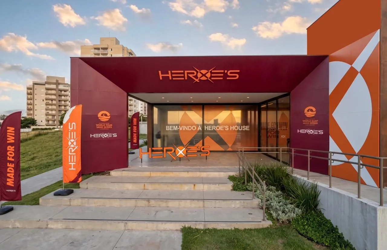Entrada da Heroes House, com pórtico vermelho e a chamada da marca aplicada na parede